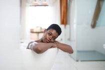 Porträt einer lächelnden afrikanisch-amerikanischen Frau im Badezimmer, die sich in der Badewanne entspannt. häuslicher Lebensstil, selbstgepflegte Freizeit zu Hause genießen. — Stockfoto