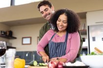 Feliz casal diversificado na cozinha preparando alimentos juntos cortando legumes. passar o tempo fora em casa no apartamento moderno. — Fotografia de Stock