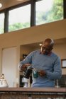 Homem americano africano sênior na cozinha moderna fazendo um café. estilo de vida aposentadoria, passar o tempo sozinho em casa. — Fotografia de Stock