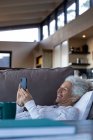 Felice donna caucasica anziani posa e utilizzando smartphone nel soggiorno moderno. stile di vita di pensione, trascorrere del tempo da solo a casa. — Foto stock