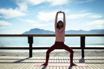 Mixed race woman practicing yoga on sunny day by seaside. healthy lifestyle, enjoying leisure time outdoors. — Stock Photo