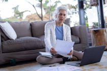 Ältere kaukasische Frau im Wohnzimmer auf dem Boden sitzend und mit Laptop. Lebensstil im Ruhestand, Zeit allein zu Hause verbringen. — Stockfoto