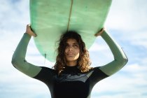 Змішана расова жінка тримає дошку для серфінгу в сонячний день на пляжі. здоровий спосіб життя, насолоджуючись дозвіллям на відкритому повітрі . — стокове фото