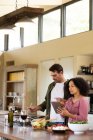 Happy diverse couple in kitchen preparing food together using tablet. spending time off at home in modern apartment. — Stock Photo