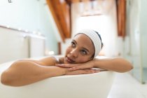 Усміхнена змішана жінка у ванній кімнаті, що розслабляється у ванній. домашній спосіб життя, насолоджуючись доглядом за дозвіллям вдома . — стокове фото