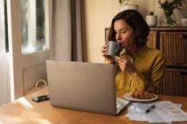 Mulher caucasiana na sala de estar, sentada à mesa a trabalhar, usando laptop. estilo de vida doméstico, trabalho remoto de casa. — Fotografia de Stock