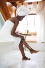 African american woman in bathroom applying body cream to her legs for skin care. domestic lifestyle, enjoying self care leisure time at home. — Stock Photo