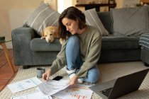 Donna caucasica in soggiorno con il suo cane domestico, seduta sul pavimento, che lavora con il computer portatile. stile di vita domestico, lavoro a distanza da casa. — Foto stock