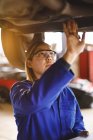 Corrida mista feminino carro mecânico vestindo macacão, inspecionando carro. proprietário de empresa independente na garagem de manutenção de carro. — Fotografia de Stock
