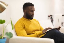 Задумчивый афроамериканец, бизнесмен, креативный сидя на диване в гостиной и работая. независимые креативные бизнесмены, работающие в современном офисе. — стоковое фото