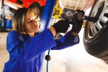 Misto gara femminile meccanico di auto indossando tuta, slacciatura ruota di auto. proprietario indipendente presso il garage di assistenza auto. — Foto stock