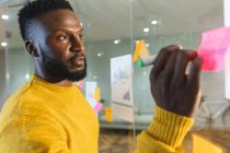 Grave afro-americano maschio business creativo brainstorming e la scrittura di appunti memo sulla parete di vetro. uomini d'affari creativi indipendenti che lavorano in un ufficio moderno. — Foto stock