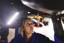 Mixed race female car mechanic wearing overalls, inspecting car. independent business owner at car servicing garage. — Stock Photo