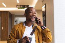 Усміхаючись афроамериканський бізнесмен творчо використовує смартфон і тримає каву. незалежні креативні бізнесмени працюють в сучасному офісі . — стокове фото
