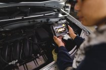 Mani di gara mista meccanico donna auto indossando tute, ispezionare auto, utilizzando tablet. proprietario indipendente presso il garage di assistenza auto. — Foto stock