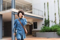Усміхнена афроамериканська бізнес-творча жінка використовує смартфон і тримає скейтборд. незалежні креативні бізнесмени працюють в сучасному офісі . — стокове фото
