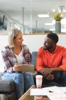 Smiling diverse female and male colleagues sitting on sofa at workplace lounge area and talking. independent creative business people at a modern office. — Stock Photo