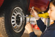 Mixed race female car mechanic wearing overalls, unbolting wheel of car. independent business owner at car servicing garage. — Stock Photo