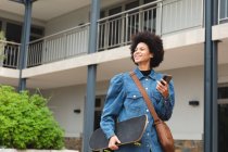 Smiling african american female business creative holding smartphone and skateboard. independent creative business people working at a modern office. — Stock Photo
