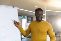 Sonriendo afroamericano negocio masculino creativo usando pizarra blanca, haciendo presentación. empresarios creativos independientes que trabajan en una oficina moderna. - foto de stock