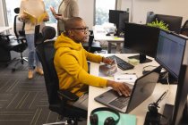Африканский американец, креативный на работе, сидит за столом, использует ноутбук. работа в творческом бизнесе в современном офисе. — стоковое фото