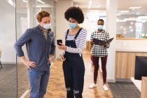 Diverse männliche und weibliche Kollegen tragen Gesichtsmasken und arbeiten per Smartphone zusammen. Arbeit im kreativen Geschäft in einem modernen Büro während der Coronavirus-Pandemie. — Stockfoto