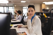 Змішана раса жіноча творчість на роботі, сидячи за столом, використовуючи комп'ютер. робота в креативному бізнесі в сучасному офісі . — стокове фото