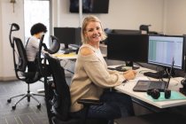 Ritratto di donna caucasica sorridente creativa al lavoro, seduta alla scrivania, che guarda alla telecamera. lavorare in attività creative in un ufficio moderno. — Foto stock