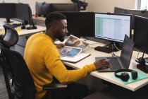Homme afro-américain créatif au travail, assis au bureau, utilisant un ordinateur portable. travailler dans une entreprise créative dans un bureau moderne. — Photo de stock