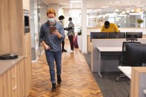 Різні чоловічі та жіночі колеги носять маски для обличчя, працюючи разом, використовуючи планшет. робота в креативному бізнесі в сучасному офісі під час пандемії коронавірусу . — стокове фото
