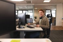 Portrait d'un homme caucasien souriant créatif au travail, assis au bureau, regardant vers la caméra. travailler dans une entreprise créative dans un bureau moderne. — Photo de stock