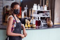 Ritratto di donna afroamericana con grembiule e maschera in piedi alla distilleria di gin. attività di distilleria di gin artigianale indipendente durante il concetto pandemico covid-19 — Foto stock