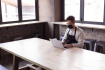 Afroamerikanerin mit Schürze und Mundschutz mit Laptop in der Gin Destillerie. unabhängige Craft-Gin-Destillerie während des Covid-19-Pandemiekonzepts — Stockfoto