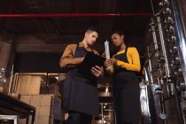 Kaukasischer Mann und afrikanisch-amerikanische Frau prüfen Gin-Produkt in Kolben in der Gin-Destillerie. Alkoholproduktion und Filtrationskonzept — Stockfoto
