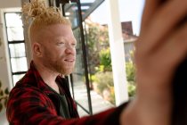 Ragionevole uomo albino americano con dreadlocks che guarda fuori dalla finestra. lavoro a distanza utilizzando la tecnologia a casa. — Foto stock