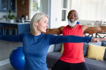 Heureux couple diversifié senior en vêtements d'exercice pratiquant le yoga ensemble, étirement. mode de vie sain et actif à la retraite à la maison. — Photo de stock