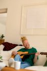 Homme souriant albinos afro-américain avec dreadlocks dans le salon à jouer de la guitare. loisirs, détente à la maison. — Photo de stock