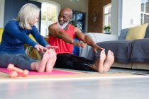 Happy senior diverse couple in exercise clothes practicing yoga together, stretching. healthy, active retirement lifestyle at home. — Stock Photo