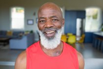 Portrait d'homme afro-américain âgé heureux en vêtements d'exercice regardant la caméra et souriant. mode de vie sain et actif à la retraite à la maison. — Photo de stock