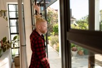 Nachdenklicher Albino-Afrikaner mit Dreadlocks, der aus dem Fenster schaut. Fernbedienung mit Technologie zu Hause. — Stockfoto