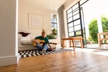 Albino-amerikanischer Mann im Wohnzimmer, der Gitarre spielt und Laptop benutzt. Freizeit mit Technik, Entspannung zu Hause. — Stockfoto