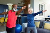 Счастливая старшая разнообразная пара в спортивной одежде практикующих йогу вместе, растяжения. здоровый, активный образ жизни на дому. — стоковое фото