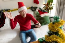 Albino afro-americano vestindo chapéu de Papai Noel fazendo videochamada com decorações de Natal. Natal, festividade e tecnologia da comunicação festividade e tecnologia da comunicação. — Fotografia de Stock