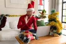 Albino-afrikanisch-amerikanischer Mann mit Weihnachtsmütze macht Videoanruf mit Weihnachtsdekoration. Weihnachten, Fest und Kommunikationstechnologie Fest und Kommunikationstechnik. — Stockfoto