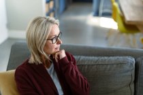 Thoughtful senior caucasian woman in living room sitting on sofa, thinking. retirement lifestyle, spending time at home. — Stock Photo
