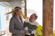 Relajante pareja caucásica de pie en una terraza junto al mar. disfrutar del tiempo libre en la casa frente a la playa. - foto de stock