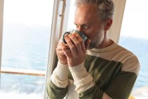 Relaxante caucasiano maduro homem bebendo café e olhando através da janela. desfrutar de tempo de lazer em casa. — Fotografia de Stock