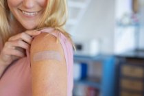 Femme caucasienne souriante montrant du plâtre sur le bras où ils ont été vaccinés contre le coronavirus. santé et mode de vie pendant la pandémie de covidé 19. — Photo de stock