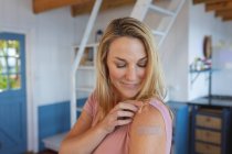 Smiling caucasian woman showing plaster on arm where they were vaccinated against coronavirus. health and lifestyle during covid 19 pandemic. — Stock Photo