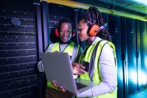 Tecnici informatici afroamericani che indossano cuffie usando laptop che lavorano nella sala server. tecnologia digitale di memorizzazione delle informazioni e rete di comunicazione. — Foto stock